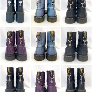 May include: Ten pairs of black leather boots with various colored accents. Each boot has a silver charm attached to the laces. The charms include a crown, a fish, a scorpion, and a skull.