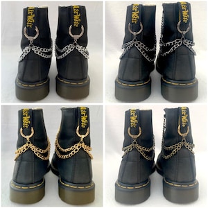 May include: Two pairs of black leather boots with gold and silver chains attached to the back of the boots. The boots have yellow stitching and the text "Air Wait" is embroidered on the back of each boot.