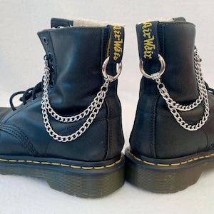 May include: Pair of black leather Dr. Martens boots with silver chains attached to the ankle loops. The boots have yellow stitching and the text "Air-Wair" is embroidered on the back of each boot.