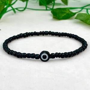 May include: A black beaded bracelet with a black and white evil eye charm.