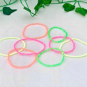 May include: A set of six neon coloured beaded bracelets. The bracelets are in shades of pink, green, and yellow.