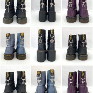 May include: Nine pairs of black, purple, and blue leather boots with various silver charms attached to the laces. The charms include a cross, a pentagram, a skull, a butterfly, and a dragon.