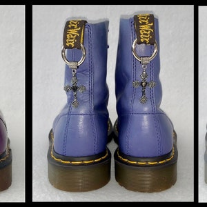May include: Three pairs of black leather boots with a silver cross charm attached to the laces. The boots are in purple, blue, and black.
