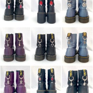May include: Nine pairs of black leather boots with various charms attached to the laces. The charms include a small Union Jack flag, a red heart, a silver key, a silver heart, a silver wine glass, a silver skull, and a silver flower.