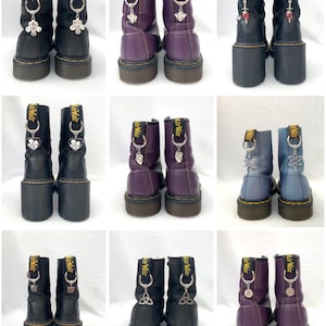 May include: Ten pairs of black leather boots with different colored laces and charms. The charms are attached to the laces and hang down. The boots have a zipper on the side and a yellow tag that says "Dr. Martens".