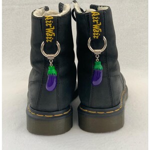 May include: Black leather boots with a faux fur lining and eggplant charms attached to the laces. The boots have a yellow stitch detail and the text "Air Weir" is embroidered on the back of each boot.