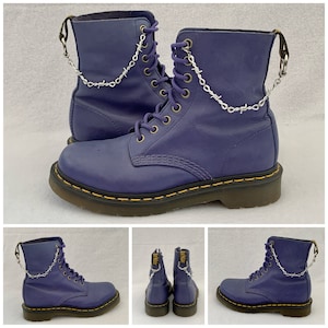 May include: A pair of indigo-colored leather boots with a silver barbed wire chain detail. The boots have a lace-up design with brass eyelets and a yellow stitched sole. The boots are approximately 8 inches tall.