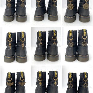 May include: Nine pairs of black leather boots with yellow stitching and gold charms. Each pair has a different charm, including a tree, moon, pentagram, skull, butterfly, and horseshoe.