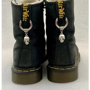 May include: Black leather boots with yellow stitching and a skull charm on each boot. The boots have a fur lining and a black pull tab with the text "Air Weir" in yellow.