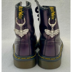 May include: A pair of black leather Dr Martens boots with silver butterfly charms attached to the laces. The boots have yellow stitching and the text "Air Wair" is visible on the back of each boot.
