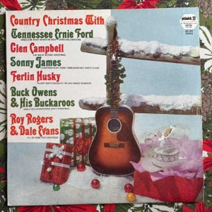 May include: A vintage vinyl record album cover titled "Country Christmas With" featuring Tennessee Ernie Ford, Glen Campbell, and others. The cover art includes a guitar decorated with greenery, snow-covered fence, and wrapped gifts. The album is a Capitol Records release.