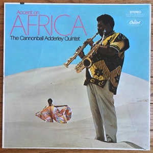 May include: A vintage vinyl record album cover featuring a man playing a saxophone in front of a desert landscape. The album title is "Accent on Africa" by "The Cannonball Adderley Quintet".