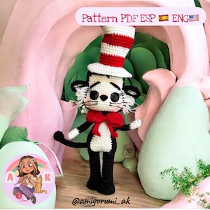 Puede incluir: Muñeco de ganchillo del Gato en el Sombrero con sombrero a rayas rojas y blancas y pajarita. El gato blanco y negro tiene bigotes blancos y está de pie frente a un fondo rosa y verde. El texto "Pattern PDF ESP ENG" está en la parte superior.