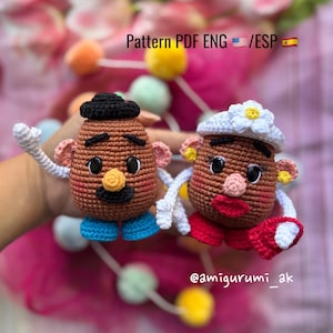 以下が含まれることがあります： ミスターポテトヘッドとミセスポテトヘッドの編みぐるみおもちゃ。おもちゃは茶色でカラフルなディテールが施されており、手をつないでいます。画像の下部に「@amigurumi_ak」というテキストがあります。