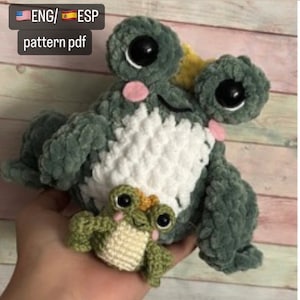 Puede incluir: Una rana verde de crochet con grandes ojos negros y vientre blanco. La rana sostiene una rana verde de crochet más pequeña con detalles amarillos. El texto "ENG/ ESP pattern pdf" es visible en la esquina superior izquierda de la imagen.