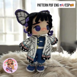 Puede incluir: Muñeca de ganchillo con cabello negro, detalles morados y alas de mariposa. La muñeca viste una chaqueta blanca con diseño azul y rosa, un atuendo azul y zapatos morados. El texto "PATTERN PDF ENG / ESP" es visible.
