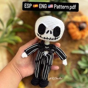 Puede incluir: Un muñeco de Jack Skellington tejido a crochet que lleva un traje a rayas blanco y negro con una pajarita negra. El muñeco tiene la cara blanca con ojos negros y una sonrisa cosida.