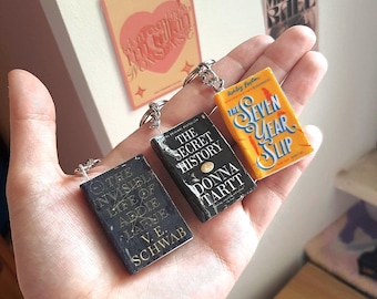 Puede incluir: Tres llaveros de libros en miniatura con las portadas de The Invisible Life of Addie LaRue de V.E. Schwab, The Secret History de Donna Tartt y The Seven Year Slip de Ashley Poston. Cada dije rectangular incluye un anillo de metal plateado.