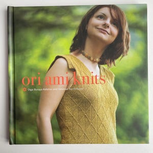 Puede incluir: Portada de libro con el título "ori ami knits" en texto rojo y blanco. La portada presenta a una mujer que lleva un top de punto amarillo mostaza con un patrón de diamantes. El fondo es verde borroso.