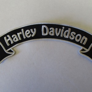 Könnte beinhalten: Schwarzer und weißer gestickter Harley Davidson Banner-Patch. Der Patch hat die Form eines Banners mit einer gewölbten Oberseite und spitzen Enden.