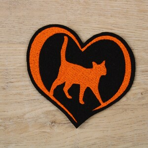 Könnte beinhalten: Orangefarbene Katzensilhouette in einem schwarzen herzförmigen Umriss. Das Herz ist orange umrandet.