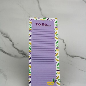 May include: A purple notepad with a white background and a pattern of green, yellow, and purple Mardi Gras masks and feathers. The notepad has a purple header that says "To Do..."