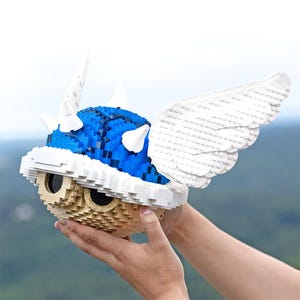 May include: A blue and white Lego model of a winged, spiky shell. The shell is made of blue Lego bricks and has white spikes and wings. The wings are made of white Lego bricks and are spread out.
