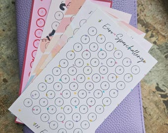 May include: A lavender textured binder featuring a stack of paper savings challenge trackers. The top tracker is white with the text Euro Sparchallenge and 300 Euro, containing rows of circles each marked with the number 5 and small colourful hearts.