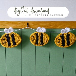 Könnte beinhalten: Eine Häkelgirlande mit sechs gelben und schwarzen Bienen mit weißen Flügeln. Die Girlande hängt an einer Holzschiene vor einer grünen Wand. Der Text "digitaler Download 6 in 1 Häkelmuster" befindet sich über der Girlande.