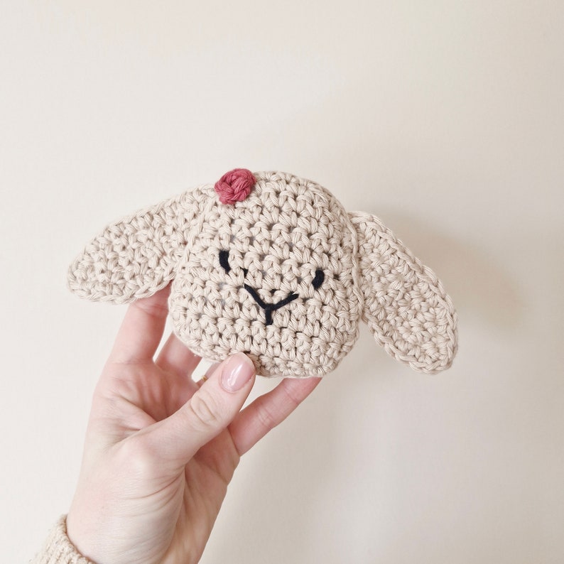 May include: A crocheted stuffed animal shaped like a bunny with a pink nose and black embroidered eyes. The bunny is beige and has floppy ears.