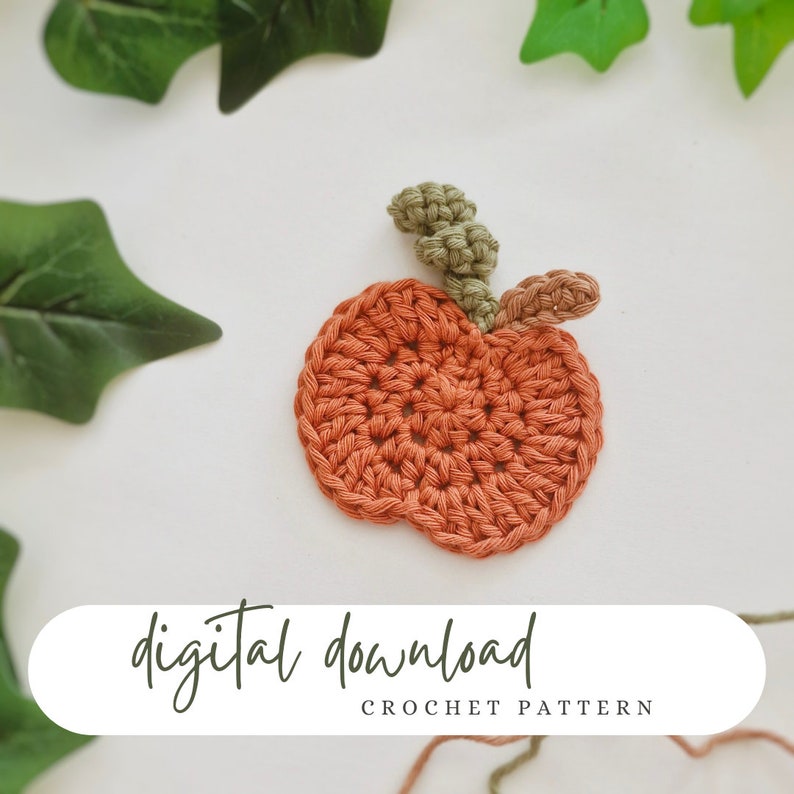 May include: A crochet pumpkin pattern, with a digital download label. The pumpkin is orange with a green stem and leaves. The pattern is for a small pumpkin, perfect for fall crafts.