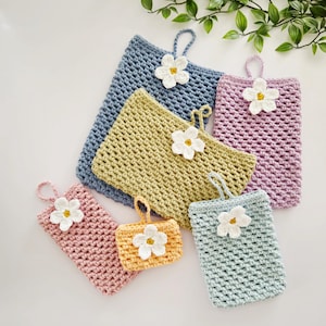May include: A collection of six rectangular crochet pouches in various sizes and colours, including blue, olive green, lavender, pink, yellow, and light blue. Each pouch features a white crocheted flower with a yellow centre and a small loop.