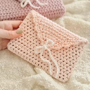 Puede incluir: Dos bolsos hechos a mano de ganchillo con forma de sobre en rosa suave. El bolso delantero est&aacute; enfocado, con un borde festoneado y un cierre de lazo de hilo blanco. El bolso de fondo tiene un dise&ntilde;o similar, ligeramente desenfocado.