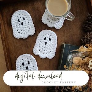 Könnte beinhalten: Weiße gehäkelte Geisteruntersetzer mit schwarzen Augendetails sind auf einem Holztablett mit einer Tasse Kaffee angeordnet. Das Bild enthält auch ein Buch und Trockenblumen. Der Text auf dem Bild lautet "digital download CROCHET PATTERN."