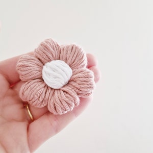 May include: A pink and white crocheted flower with a white center. The flower is made of yarn and has a soft, fluffy texture.