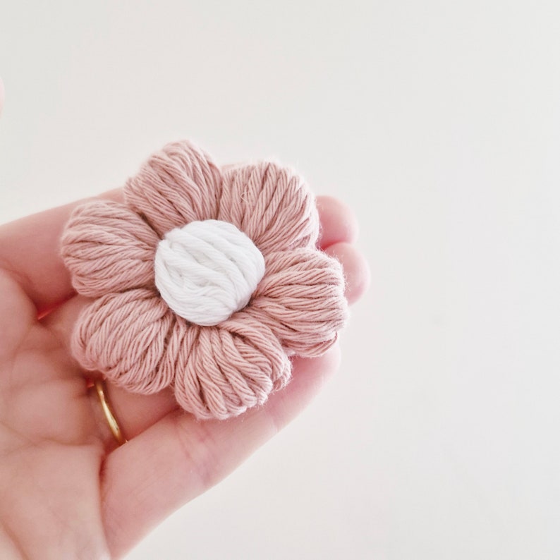 May include: A pink and white crocheted flower with a white center. The flower is made of yarn and has a soft, fluffy texture.