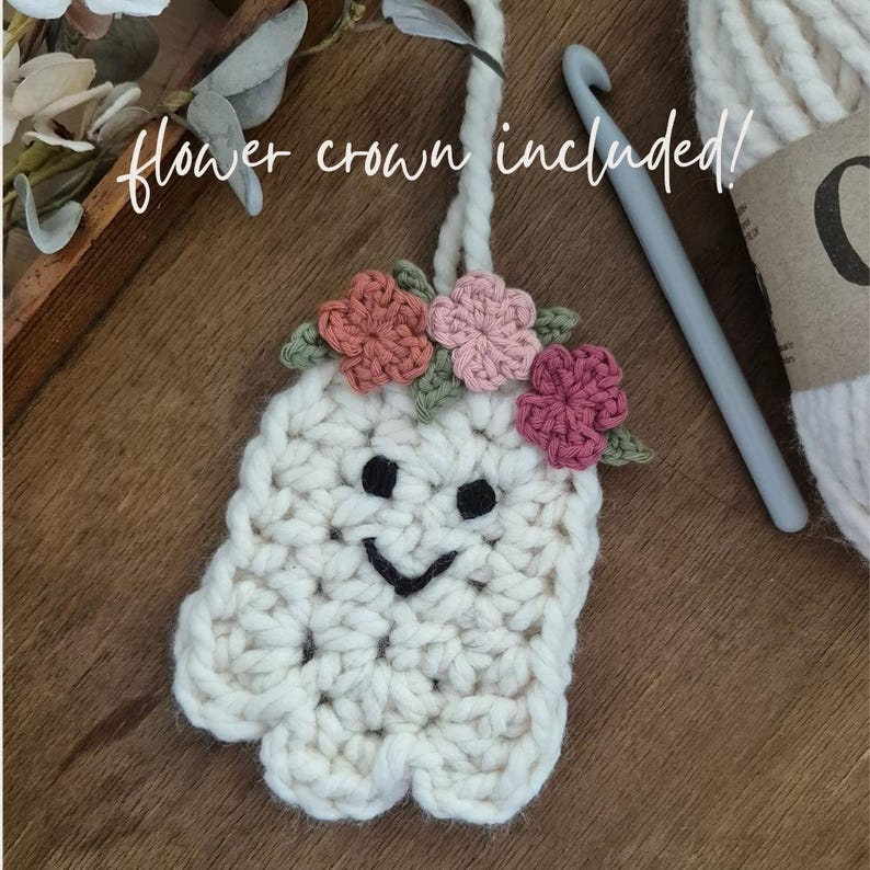 May include: A handmade, off-white crochet ghost with a smiling face and a flower crown. The ghost has a loop for hanging. The text "flower crown included!" is written in cursive. A crochet hook and yarn are in the background.