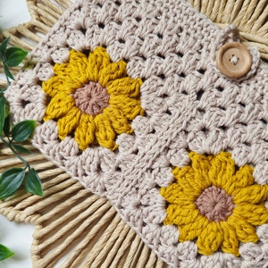 May include: A crocheted beige pouch with two yellow and brown crocheted sunflowers. The pouch has a wooden button closure.