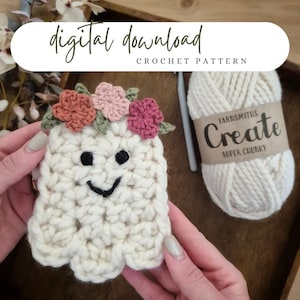 May include: A crocheted ghost with a floral crown, held in hands. The ghost is off-white with a smiling face. The text "digital download CROCHET PATTERN" is at the top. A ball of yarn and a crochet hook are also visible.