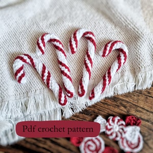 May include: Four handmade crochet candy canes with red and white stripes are arranged on a textured white surface. The candy canes are curved and detailed, showcasing a festive holiday theme. Additional crochet candies are visible in the background.