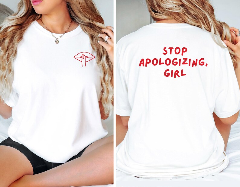 May include: White t-shirt with a red lip and finger graphic on the front. The back of the shirt has the text "STOP APOLOGIZING, GIRL" in red. The shirt is made of a soft material.