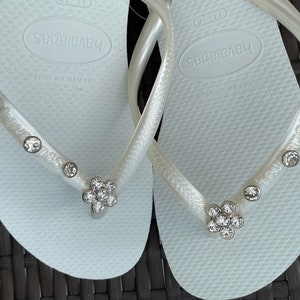 May include: A pair of white flip-flops with rhinestones and the word "havaianas" on the straps.