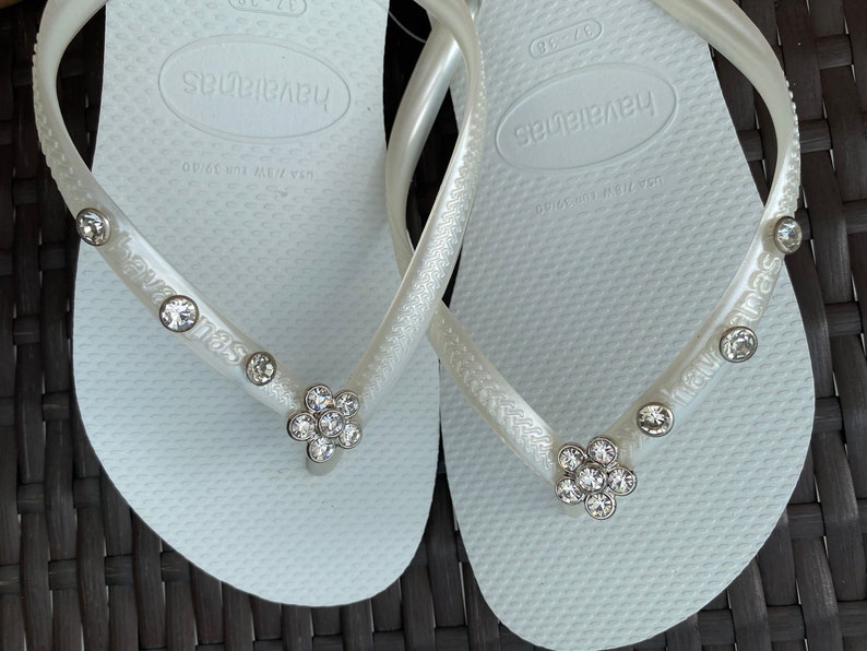 May include: A pair of white flip-flops with rhinestones and the word "havaianas" on the straps.