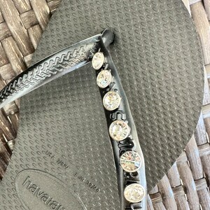 May include: Black flip-flops with a row of rhinestones on the strap. The flip-flops have the text "havaianas" and "37-38" printed on the sole.