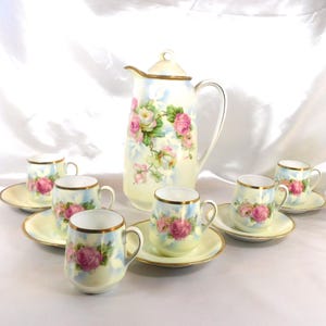 May include: A vintage porcelain tea set with a cream-colored base and delicate pink rose floral pattern. The set includes a teapot and six cups and saucers.