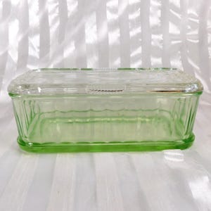Könnte beinhalten: Eine rechteckige Glasschale im Vintage-Stil mit einem durchsichtigen Deckel. Die Schale ist hellgrün und hat ein geripptes Design an den Seiten. Der Deckel ist transparent und hat einen Griff. Die Schale wird wahrscheinlich zur Aufbewahrung von Lebensmitteln verwendet.