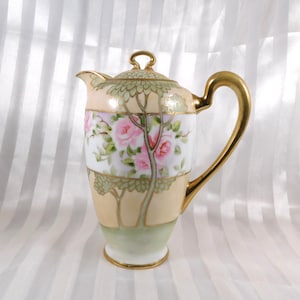 Peut inclure: Une cafetière en porcelaine ornée d'un motif peint à la main représentant des roses roses et des arbres verts sur un fond crème et vert pâle. L'objet comprend une anse dorée, un couvercle assorti avec un bouton en boucle et des bordures dorées.