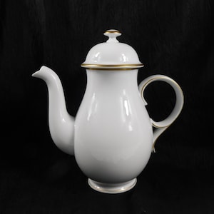 May include: White porcelain coffee pot with a rounded body, curved spout, and a loop handle. The lid and base are trimmed with gold accents. The pot has a classic, elegant design, suitable for serving coffee or tea.