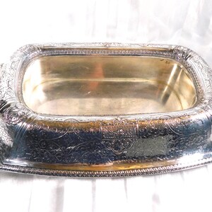 May include: A rectangular silver-plated serving tray with ornate floral and scrollwork detailing. The tray has a raised rim and handles on each side. The interior is a polished silver color. The tray is likely vintage and suitable for serving food or displaying items.
