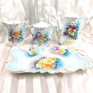 Könnte beinhalten: Ein Vintage-Porzellan-Teeservice mit Teekanne, Sahnekännchen, Zuckerdose mit Deckel und Serviertablett. Das Set ist mit farbenfrohen Blumenmustern in Gelb-, Orange-, Lila- und Blautönen bemalt und mit Gold verziert.